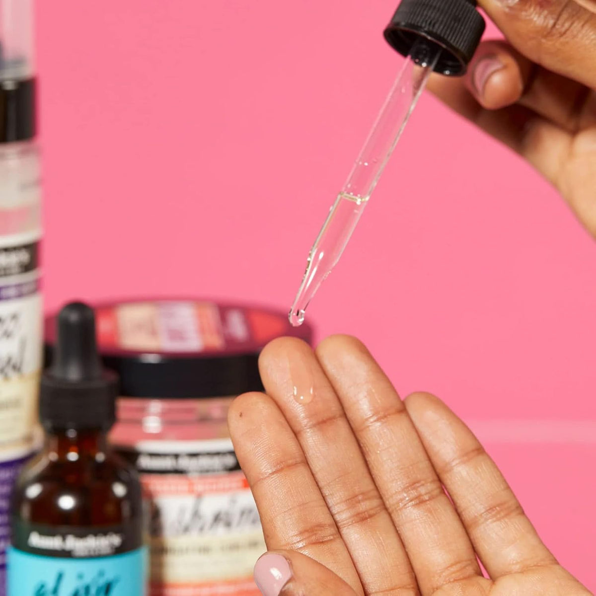 Close-up of a hand dripping Aunt Jackie's Elixir Biotin Rosemary Hair and Scalp Oil from a pipette onto the fingertip.