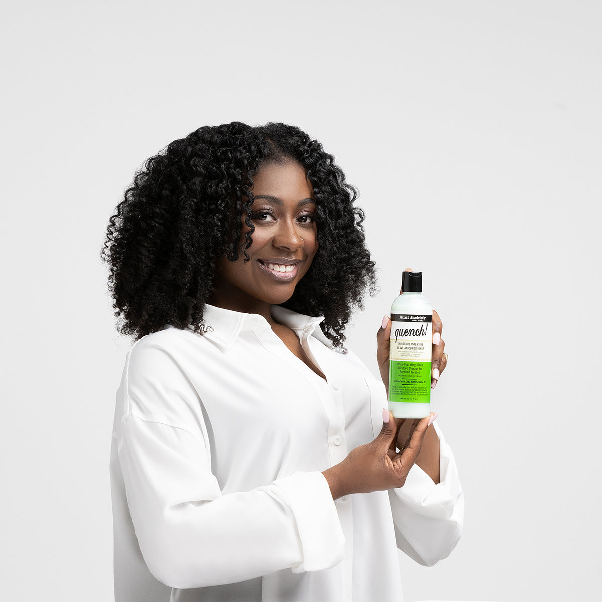 Clutch holding a pale green bottle of Aunt Jackie's Quench Moisture Intensive Leave-In Conditioner with a black cap.