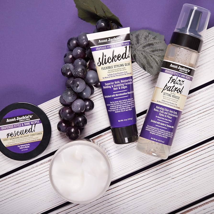 Four hair products from Aunt Jackie's Grapeseed Style & Shine Recipes range: Rescued! Conditioner, Slicked! Styling Glue and Frizz Patrol Mousse, accompanied by dark grapes.