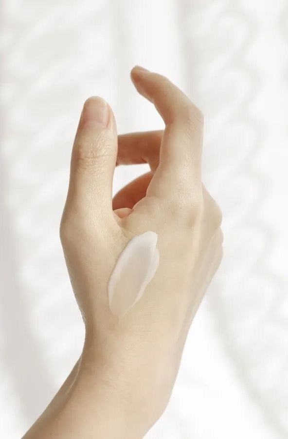Hand with applied Beauty of Joseon Dynasty Cream 50ml shows creamy texture in soft lighting against white background.