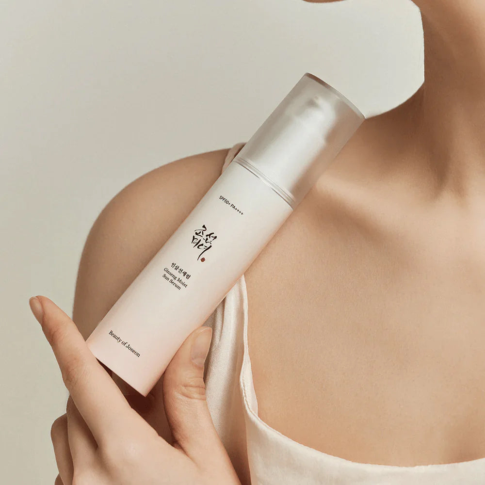 Woman's hand holds Beauty of Joseon Ginseng Moist Sun Serum 50ml against bare shoulder in soft, natural light.