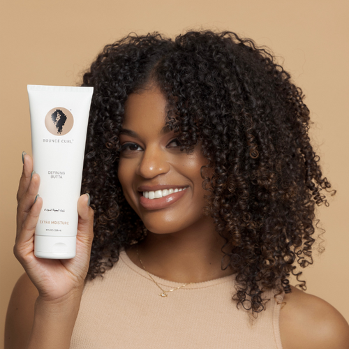 Person with curls holds tube of Bounce Curl Defining Butta.