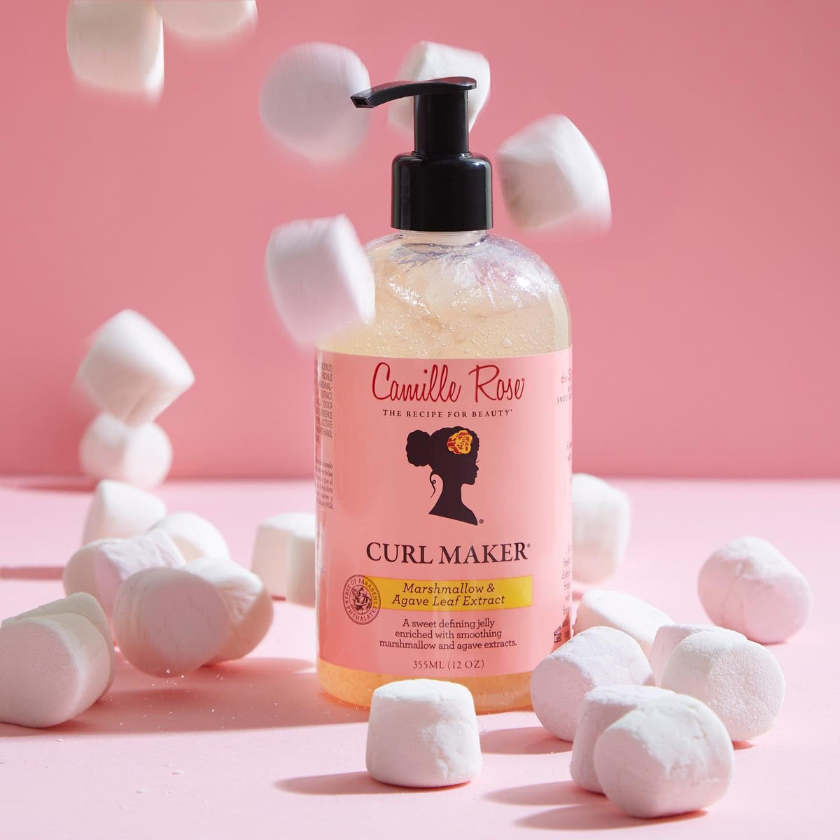 Product photograph of Camille Rose Curl Maker hair gel. The bottle is placed on a pink background with small white marshmallows falling around it.