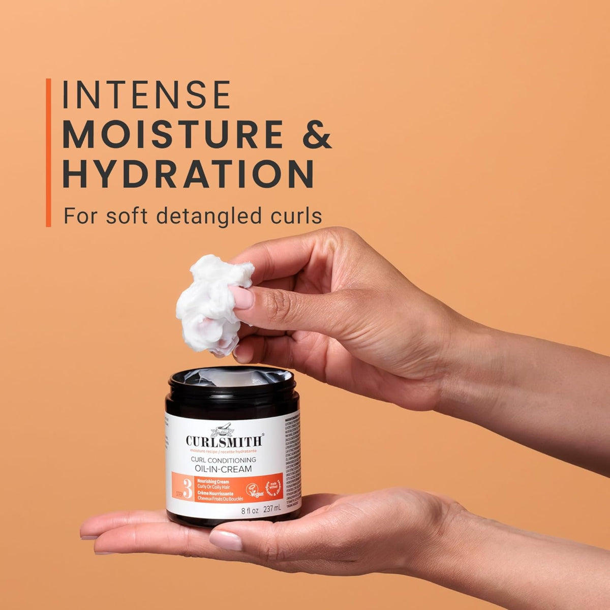 Curlsmith Curl Conditioning Oil-In-Cream cream in black jar, hand takes creamy product for intense hydration of curls.