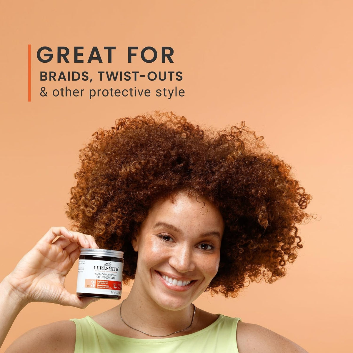Woman with curly auburn hair smiles and holds Curlsmith Curl Conditioning Oil-In-Cream, ideal for braids and twist-outs.