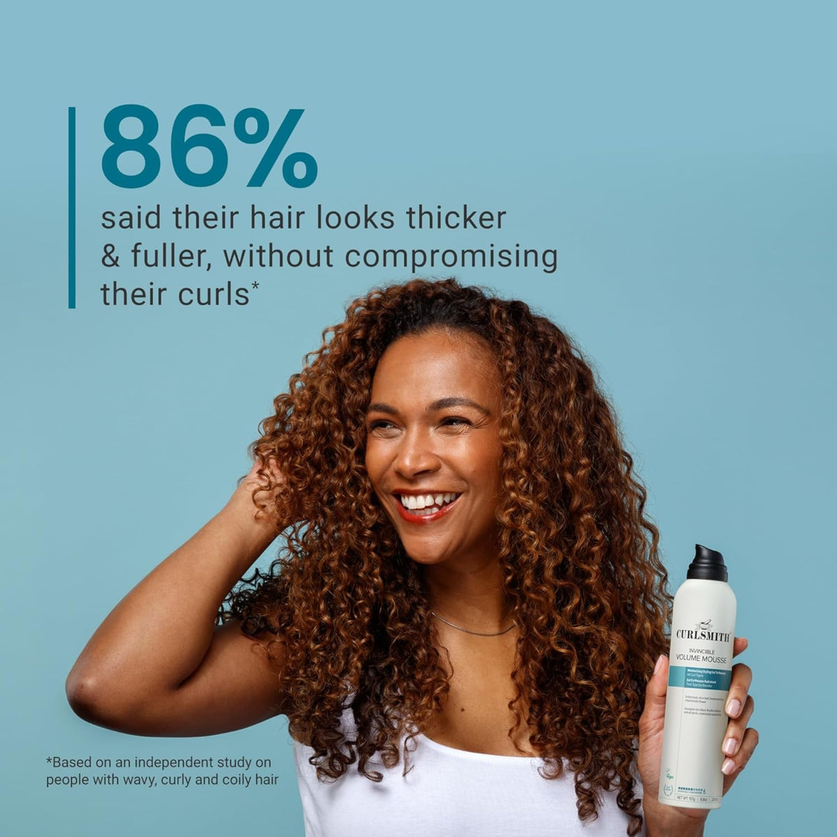 Woman with curly hair smiles and holds Curlsmith Invincible Volume Mousse - 86% experienced thicker, fuller curls.