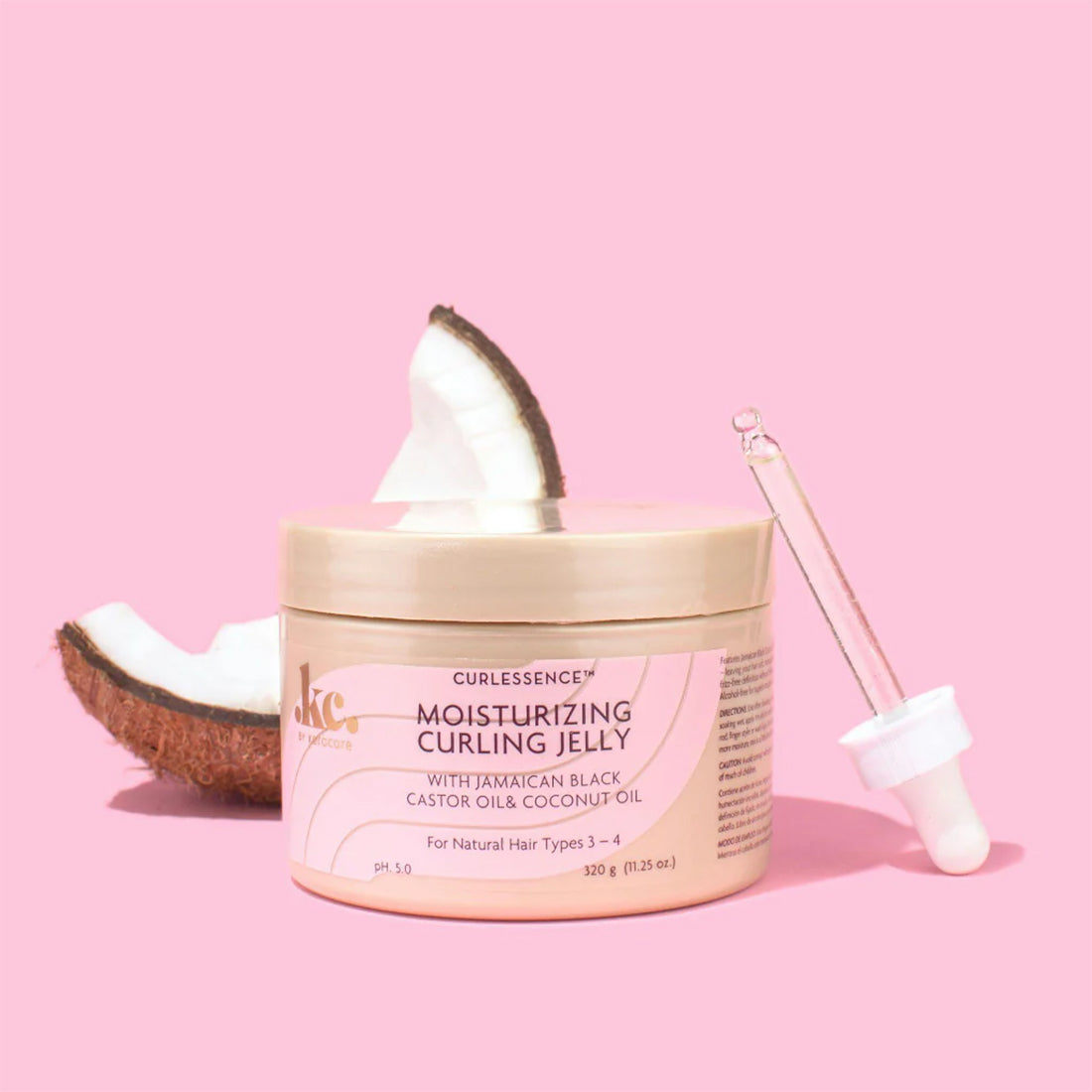 Container of KeraCare Curlessence Moisturizing Curling Jelly on a pink background, accompanied by pieces of a fresh coconut and an eyedropper. Highlights the use of coconut oil in the product.