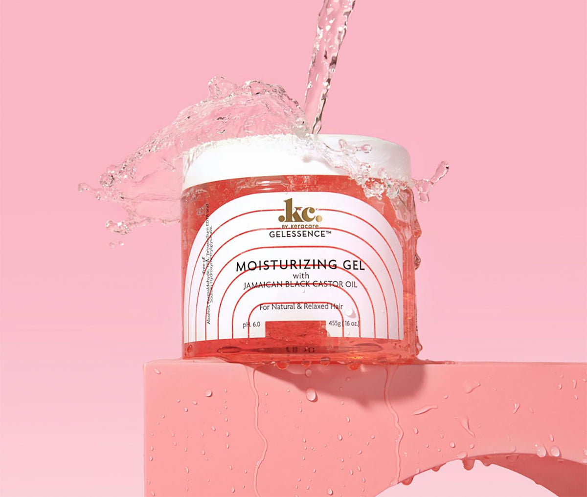 Clear container with KeraCare Gelessence Moisturizing Gel. Water splashes up around the container on a pink background, highlighting the moisturizing properties of the product.
