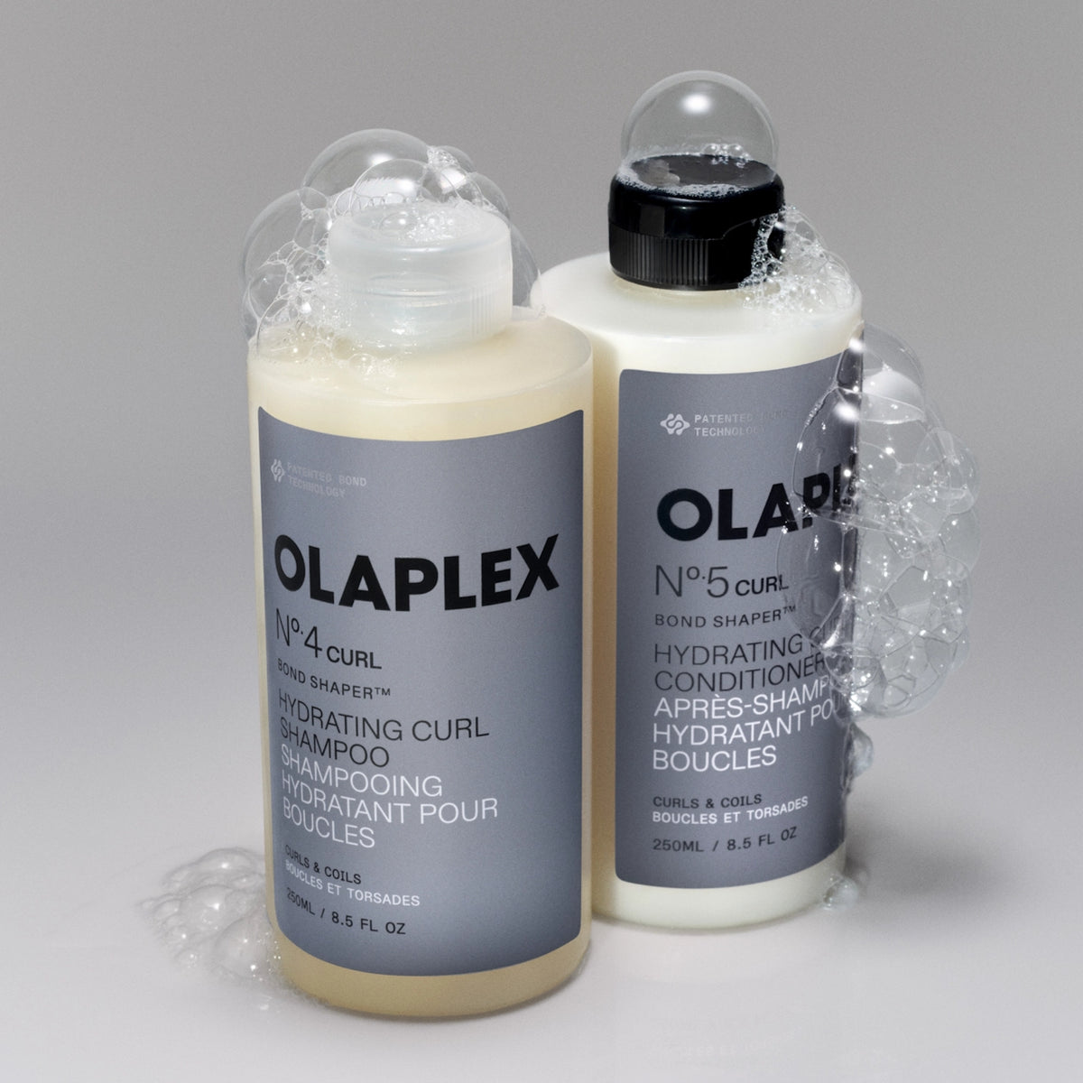 Olaplex No. 4 Curl shampoo and No. 5 Curl conditioner with foam against a gray background.
