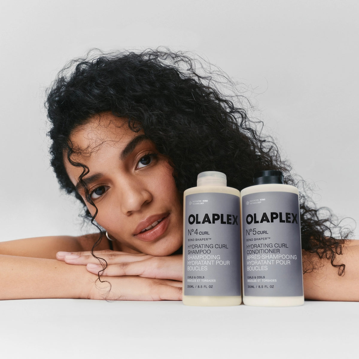 Woman with curly hair next to Olaplex No.4 Curl shampoo and No.5 Curl conditioner for curls.