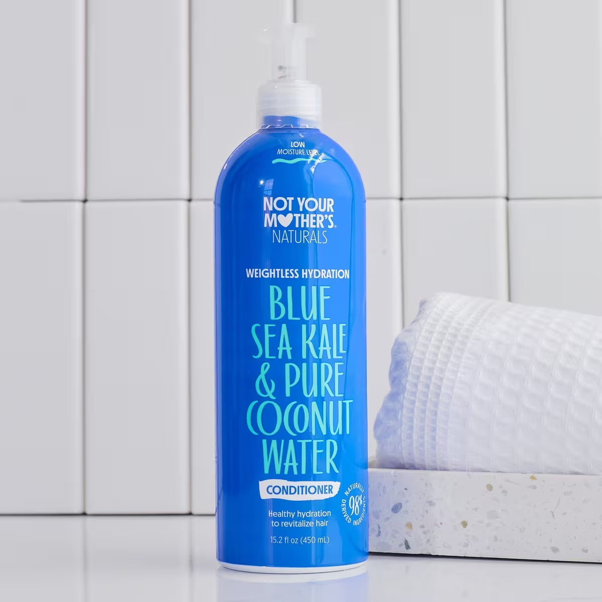 A blue bottle of Not Your Mother's Naturals Blue Sea Kale & Pure Coconut Water Weightless Hydration Conditioner in front of a white tiled background.