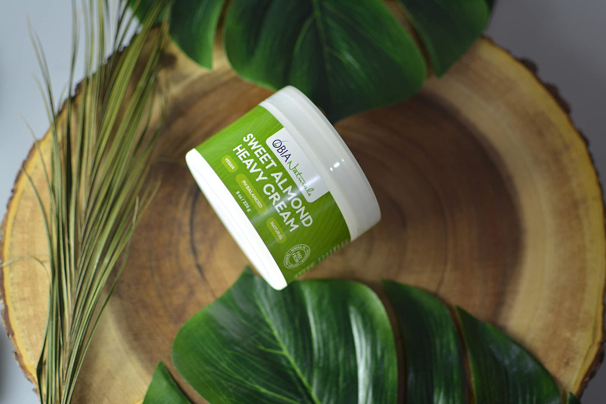 OBIA Naturals Sweet Almond Heavy Cream (226g) presented with green leaves on a wooden board.