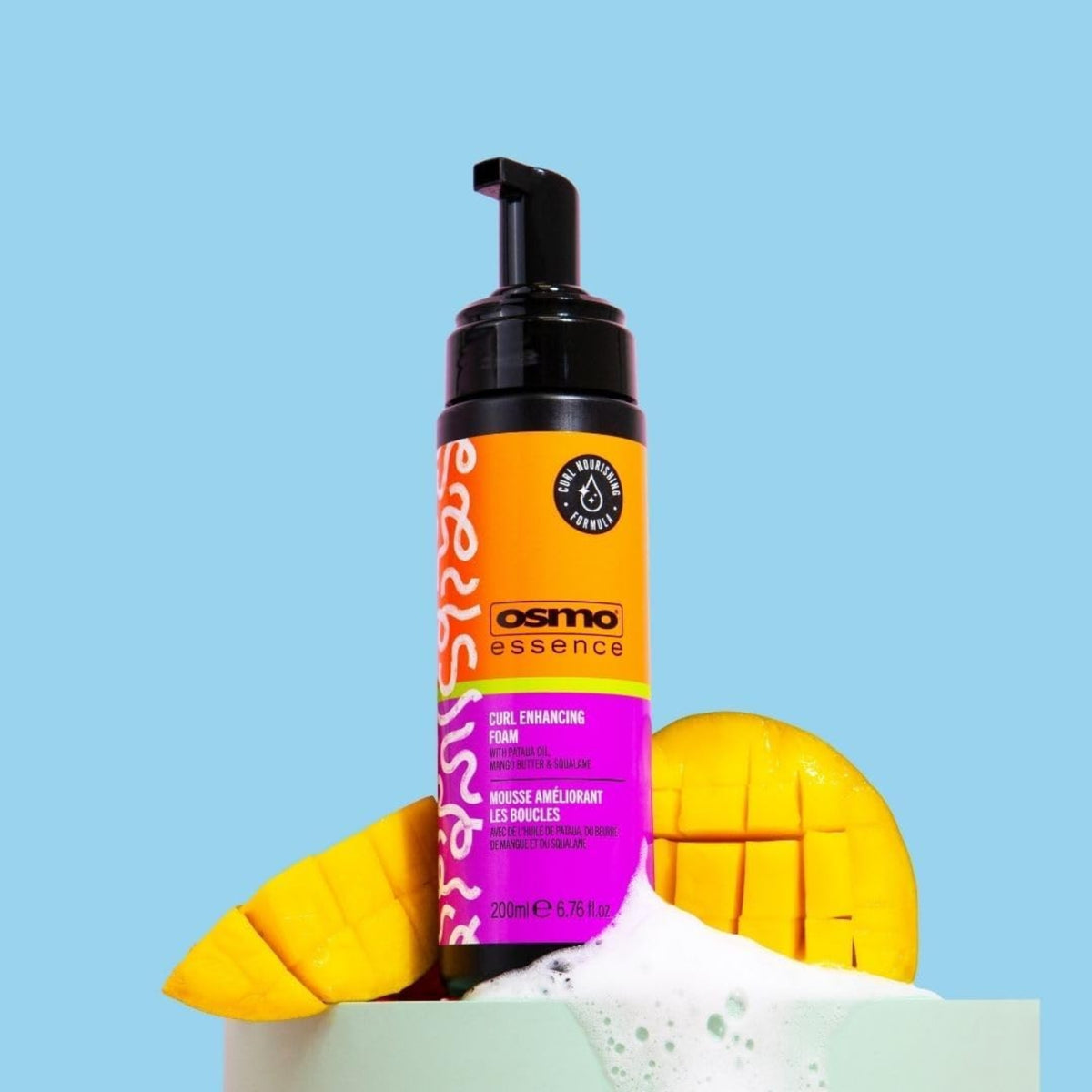Osmo Essence Curl Enhancing Foam pump bottle with foam and fresh mango slices on a light blue background.