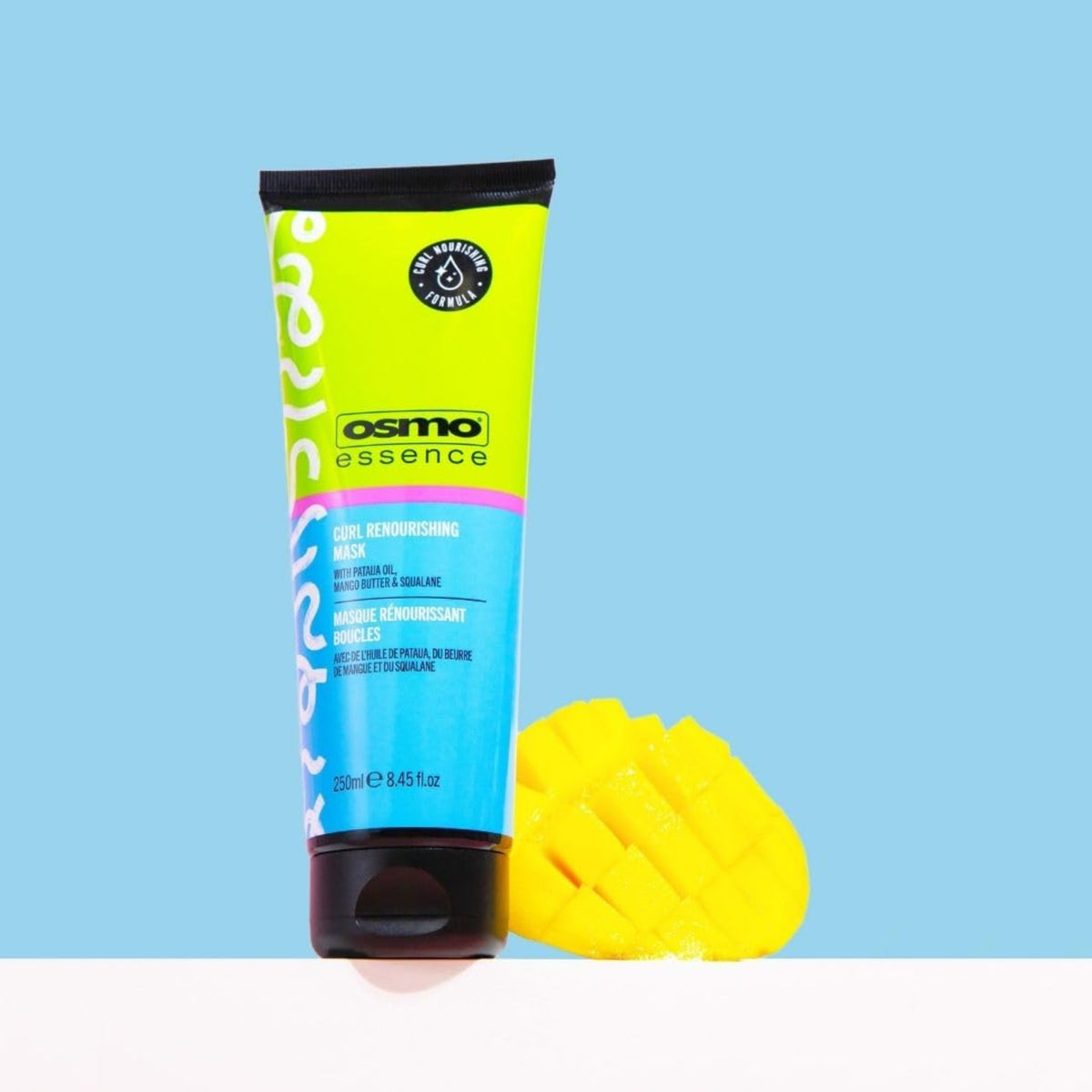 Osmo Essence Curl Renourishing Mask tube of 250 ml with a carved mango next to it on a light blue background.