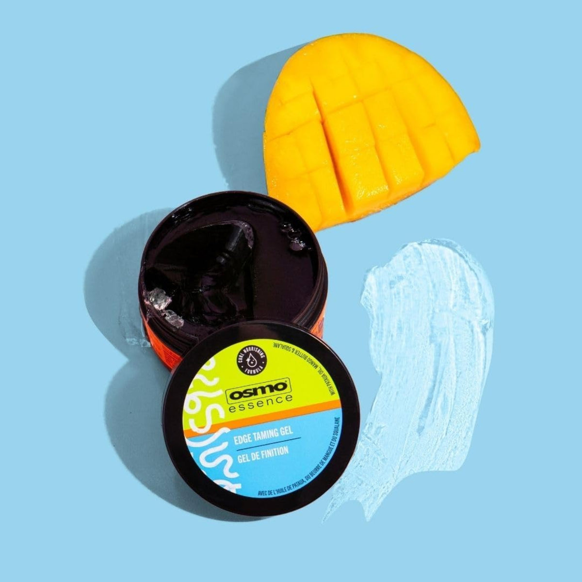 Osmo Essence Edge Taming Gel in open black can next to carved mango on light blue background.