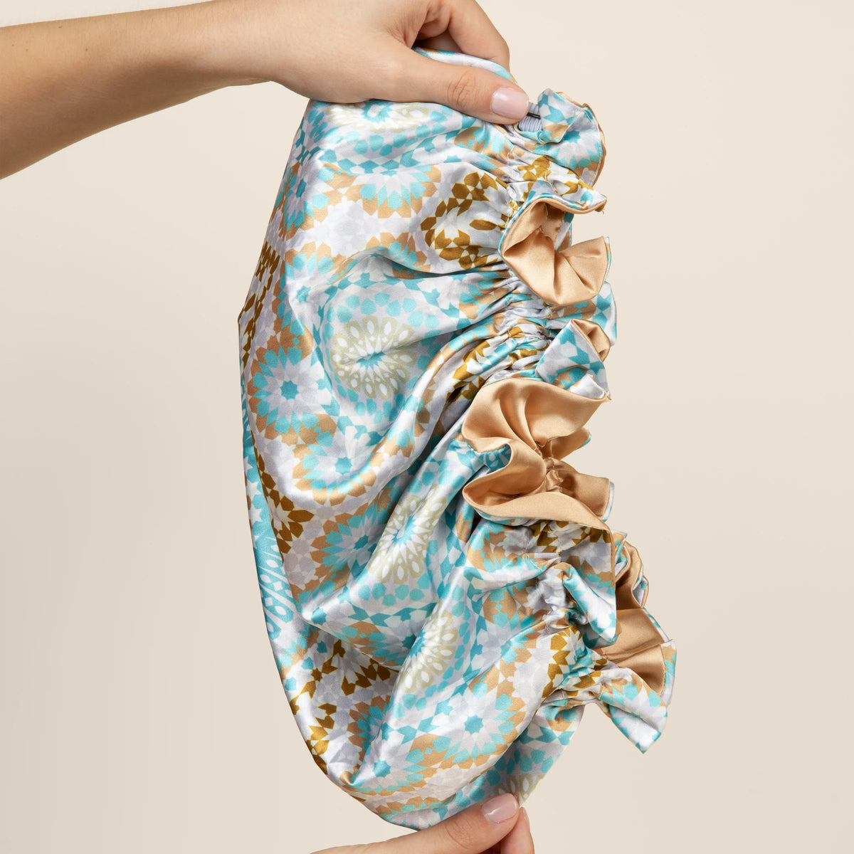 Bounce Curl Reversible Satin Hair Bonnet in mint green, gold and white pattern is held up between two hands.