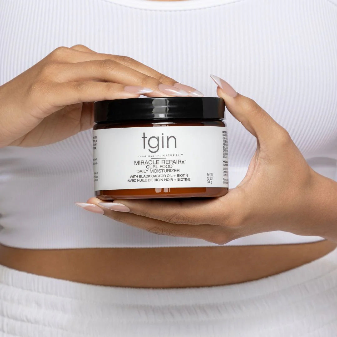 Jar of TGIN Miracle RepairX Curl Food 340gr is held in hands in front of white top, shows daily moisturizer for curls.